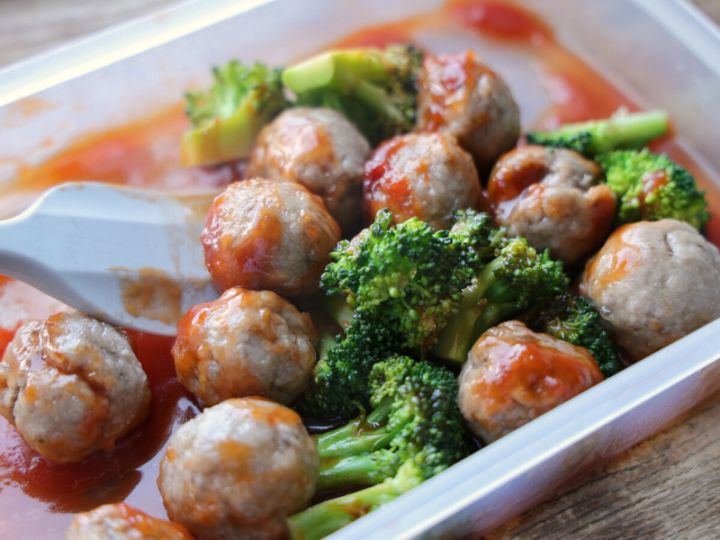 電子レンジ加熱後にとろみのついたケチャップだれのミートボールとブロッコリーをスプーンで混ぜる様子