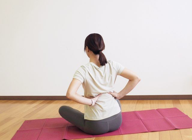 腰に手を当てあぐらで座る女性の後ろ姿