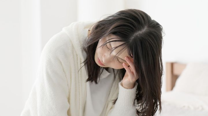体調不良 こめかみを抑えてうずくまる女性