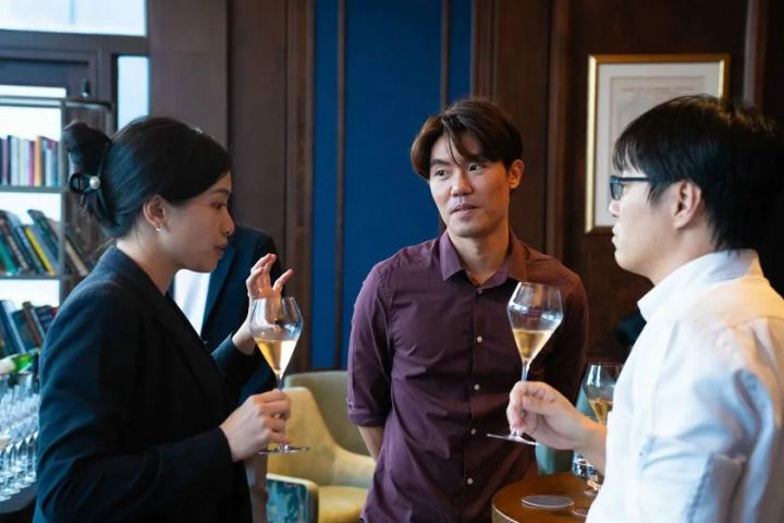 イベント懇親タイム中にシャンパングラスを手にした3名の参加者が立ち話で意見交換している近接ショット