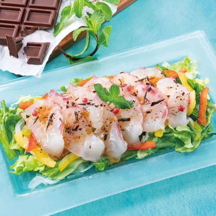 チョコミント風味のドレッシングをかけた白身魚のカルパッチョ風サラダ仕立て。透明プレートに野菜と魚介を盛り付け、ミントの葉とチョコチップで飾り付け