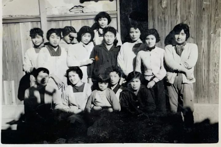 昭和期撮影と思われる南出メリヤス工場の女性従業員約13名が建物前で並んだモノクロ集合写真。創業当時の職場の様子を伝える歴史的記録
