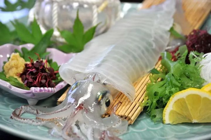 ヤリイカまたはスルメイカの姿造り刺身。竹すのこの上に透明感のある胴身と頭部を丸ごと盛り付け、わさび・紅たで・海藻・レモンを添えた一皿