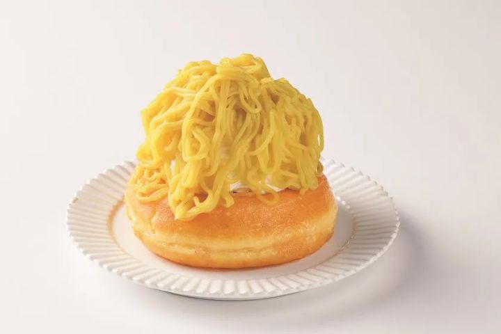 丸いドーナツ型のパン台の上に黄色いモンブランクリームを山盛りに絞り出したスイーツ、白い皿に乗せてシンプルな背景で撮影