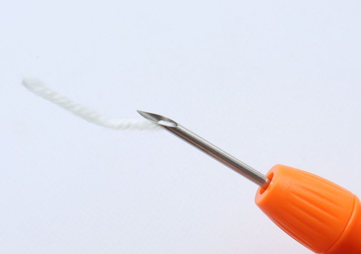 スレダーを使ってニードルペンに白い毛糸を通している様子