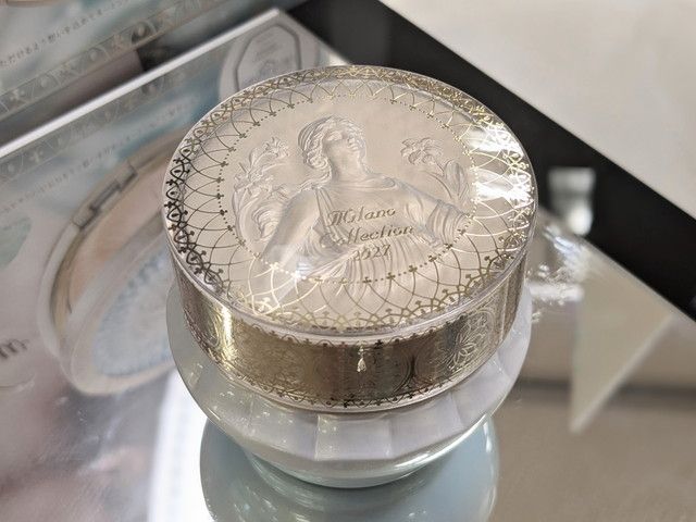 ミラノコレクション ドレスアップクリーム2027の容器アップ。蓋に女神とユリの刻印、レース調のデザインが施されている