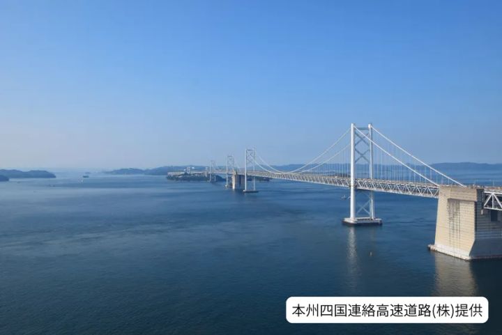瀬戸内海に架かる大橋（与島付近）を遠景から撮影した写真。本州四国連絡高速道路提供のクレジット入り、穏やかな海面と複数の橋脚が続く構図。