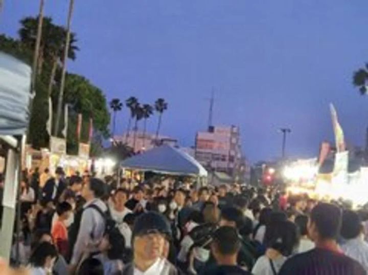 夕暮れ時の野外グルメイベント会場内の様子で、照明が灯った飲食店ブースが並ぶ通路に大勢の来場者が密集している混雑風景