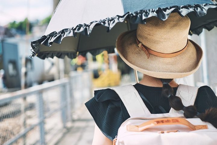 帽子をかぶり日傘をさして歩く女性