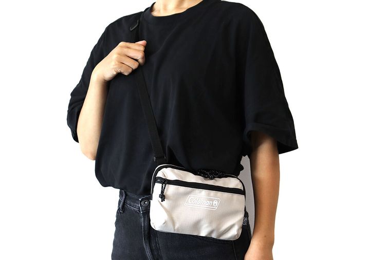 黒い半袖Tシャツの女性が右手でストラップを持ちColemanベージュのミニショルダーを斜め掛けする着用イメージ