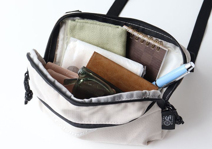 Colemanミニショルダーの中身。緑のタオル・茶色の財布・グリーンのサングラス・茶色のリングノート・青いペンが入っている