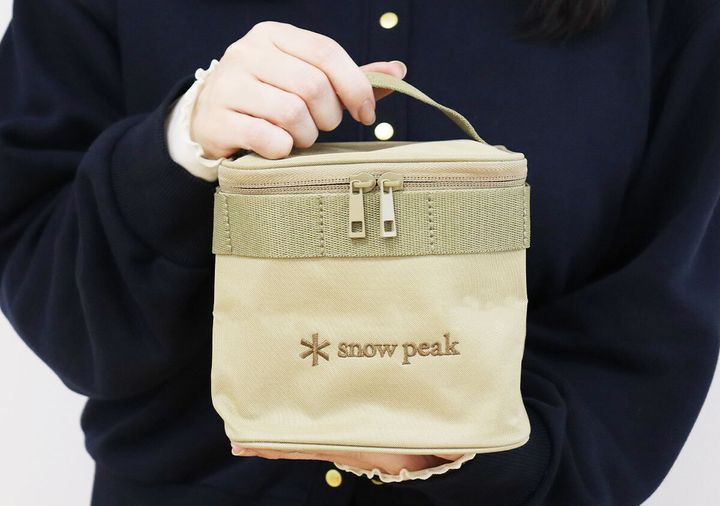 ネイビーセーターの女性がsnow peakのベージュバニティポーチを両手で胸の前に抱える着用イメージ