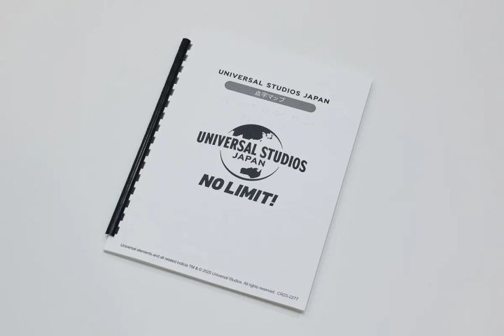 ユニバーサル・スタジオ・ジャパンが視覚障がいゲスト向けに提供する点字マップの冊子表紙で、USJロゴとNO LIMIT!のスローガンが印字されたA4判冊子の斜め俯瞰ショット