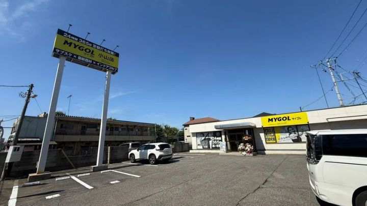 マイゴル小山店の駐車場と外観全景。24時間365日定額打ち放題を謳うポール看板と店舗建物全体が写り、広い駐車スペースが確認できる