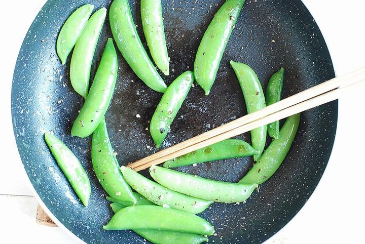 黒いフライパンでバターと一緒に炒められているスナップエンドウを菜箸で動かしている俯瞰写真