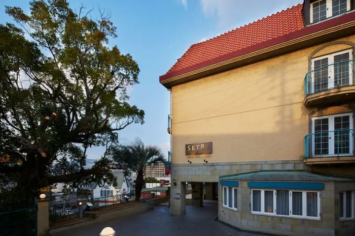 セトレグラバーズハウス長崎の外観。赤い瓦屋根と淡いベージュの洋館風建物にSETREの看板が掲げられ、大木とバルコニーが異国情緒ある雰囲気を示す施設外観写真