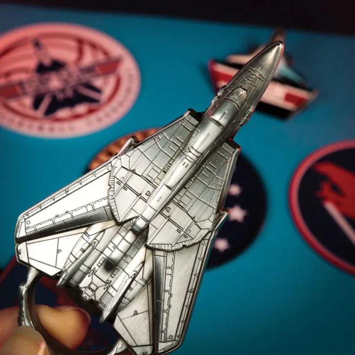 F-14トムキャット型キーホルダーをアップで手持ち撮影したショット。シルバー色の精巧なパネルライン彫刻と可変翼形状が確認でき、背景にコレクタブルコイン各種が散りばめられている
