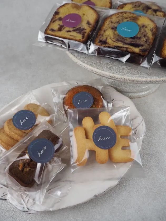hueブランドのマーブルパウンドケーキ・クッキー・マフィン・ブラウニーなど複数種の手作り焼き菓子を個包装で並べた商品ショット。ロゴシールで統一されたパッケージ