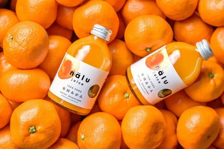 nalu juiceブランドの有田みかん100%ピュアジュース瓶2本を、みかんの山の上に置いた商品写真。和歌山産・農家直製の表記ラベルが読める