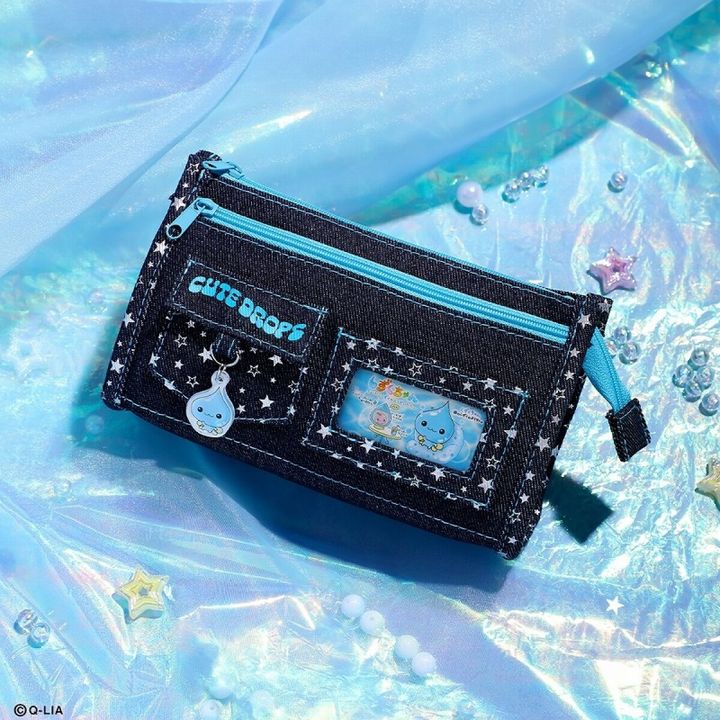 ホログラム調の水色布地の上に、星柄ステッチが入ったブラックデニムの2ポケットポーチ、しずくちゃんのアクリルチャームとメッセージカードが付いた斜めアングル写真