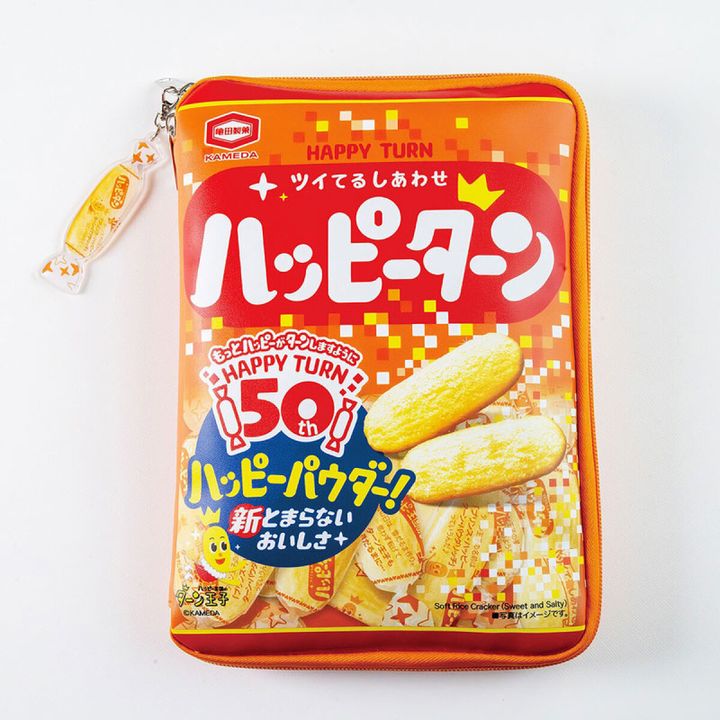 黒背景に、ハッピーターン50周年パッケージデザインを再現したオレンジ・赤のじゃばらポーチが置かれ、ファスナーにキャンディ型の包み紙そっくりなアクリルチャームが付いた俯瞰写真