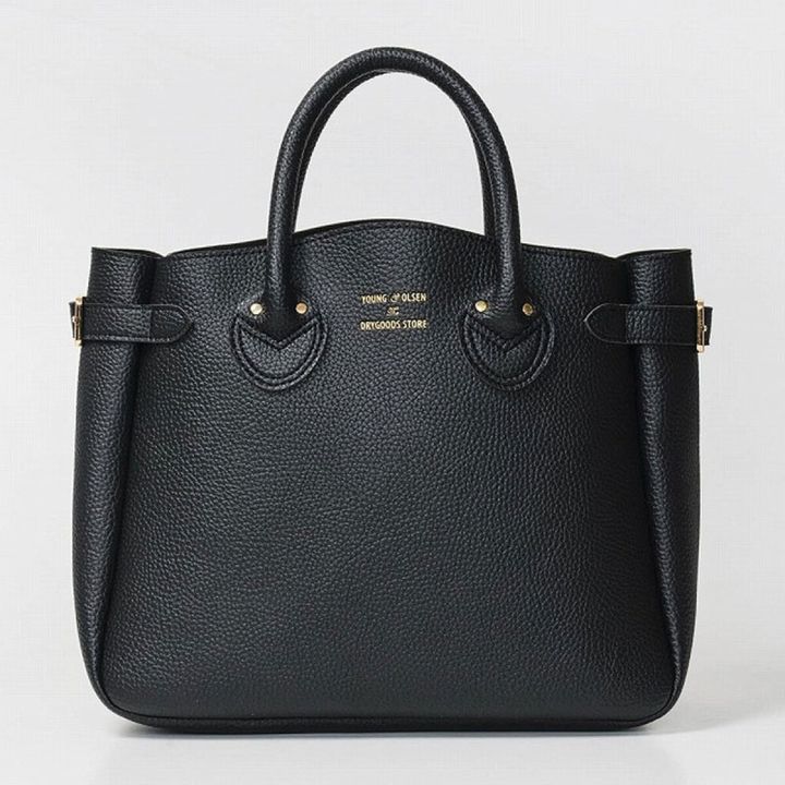 ライトベージュ背景に、シボ革風BLACKレザートートバッグを正面から撮影、ゴールドのYOUNG ＆ OLSEN DRYGOODS STOREロゴと両サイドのバックル付きベルトが見える写真