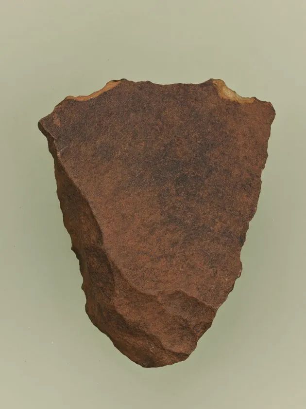 旧石器時代の打製石器（礫器）の単体撮影。赤褐色の石材に打撃による剥離痕が確認でき、盾形に近い輪郭を持つ標本写真