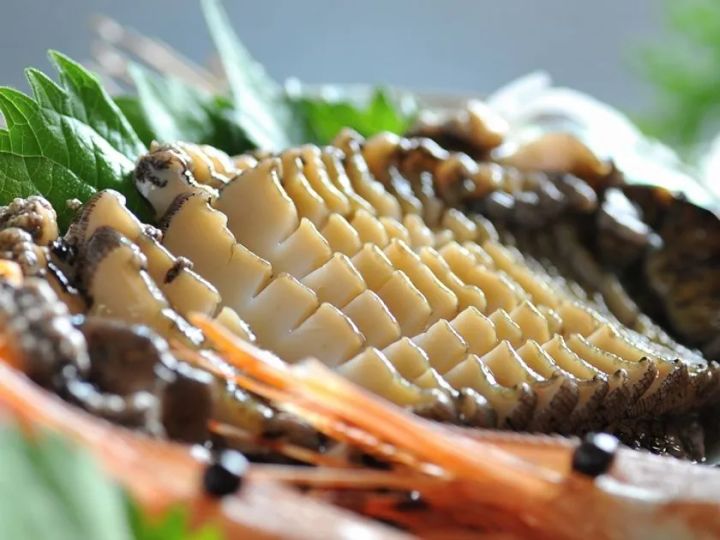 大きなサザエ（または鮑類）の壺焼き断面アップと伊勢海老の身をとらえたクローズアップ料理写真。貝の筋目と光沢ある身の質感が鮮明に写る