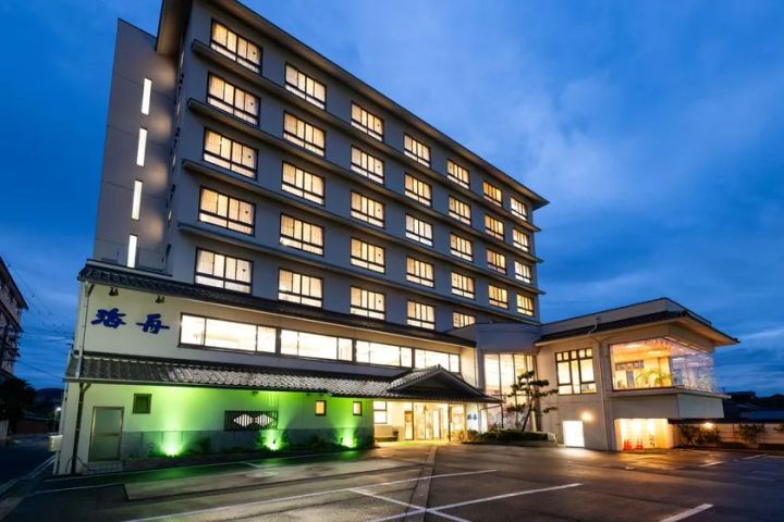 旅館「海舟」の外観を夕景時に撮影した写真。7〜8階建ての白いビル型建物で、正面エントランスがグリーンのライトアップで照らされ、「海舟」の看板が青字で掲示されている