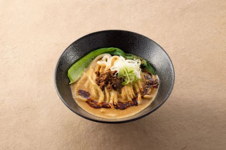 絵空事Fビレッジ店のグルテンフリー玄米うどん・担担麺風メニュー。黒い丼鉢に太麺・挽き肉・チンゲン菜・白ネギ・ラー油を盛りつけた一品。