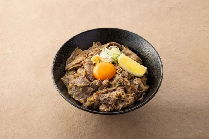 絵空事Fビレッジ店の玄米うどんを使った牛肉丼風メニュー。黒い丼鉢に薄切り牛肉・卵黄・ネギ・レモンを盛りつけた一品。
