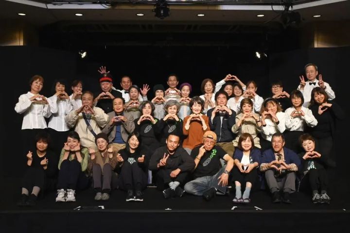 劇団すずしろの全メンバー約30名がステージ上でハートポーズをとる集合写真。シニア中心の劇団員構成がわかる黒背景のホール内での撮影。