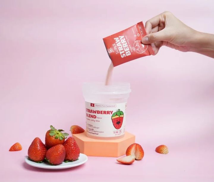 ペット用ストロベリーブレンドジェリーミックス（Strawberry Blend）の粉末をカップに注ぐシーン。スイス産ビタミン配合・プロバイオティクス訴求のサプリメント系ペット製品パッケージ