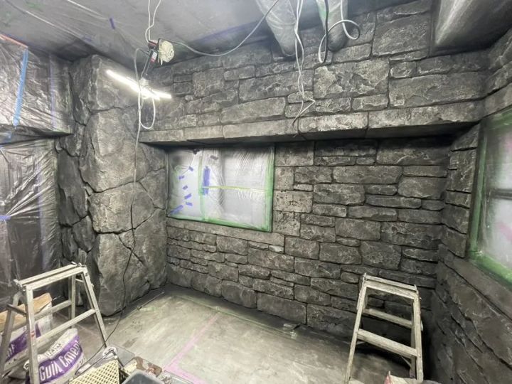 石積み風の壁面造作が施工途中の室内空間で、脚立2台と養生テープが残り、完成前の内装制作工程がわかる現場写真