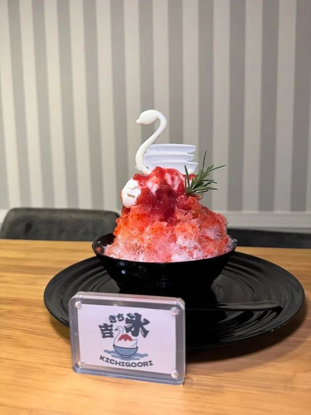 「吉氷 KICHIGOORI」ブランドのかき氷。黒い器に赤いシロップとホイップクリームを乗せ、白鳥の飾りとローズマリーで仕上げた商品写真。店名プレート付き