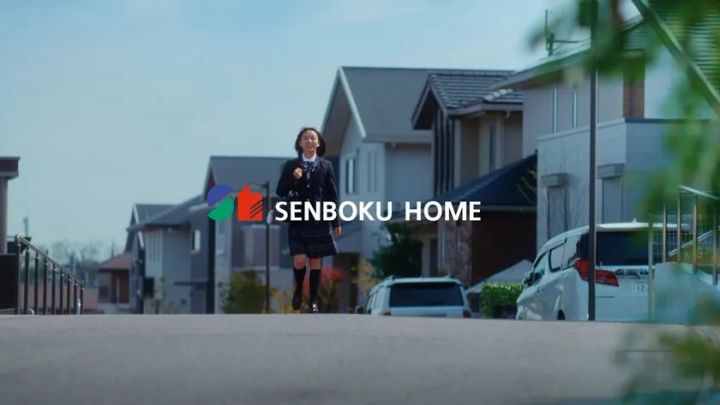 泉北ホーム（SENBOKU HOME）のロゴが重なる住宅街の路上で、制服姿の女子生徒が走り帰宅するTVCM「家族の家路」篇のワンシーン。背景に戸建て住宅が並ぶ晴天の郊外風景。