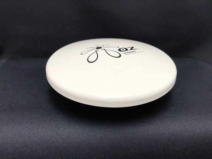 小峰無線電機のGNSSアンテナ製品「OZ」シリーズと思われる円盤型白色筐体の単体商品ショット。KOMINEブランドロゴと型番表記が天面に入り、黒背景で撮影された正面斜め上からのカット