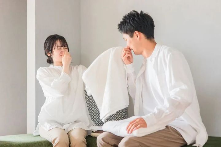 白いタオルのニオイに顔をしかめる男女2人のイメージカット。部屋干し臭・洗濯物のニオイ問題を視覚的に表現したシーン写真