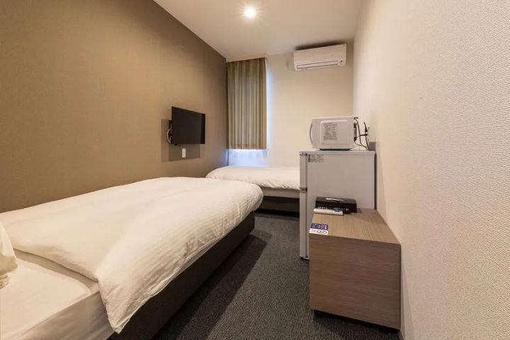 コンテナホテル客室のツインルーム内装。シングルベッド2台・壁掛けテレビ・エアコン・電子レンジ・冷蔵庫・ナイトテーブルが配置されたコンパクトな室内全体。