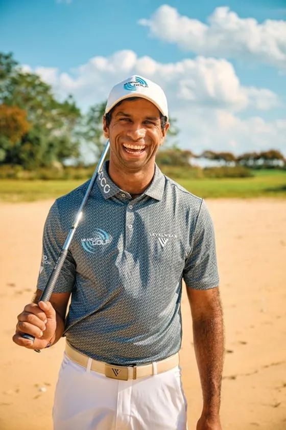 ゴルファーのアーロン・ライがECCO GOLFロゴ入りキャップとLevelwearポロシャツ着用でゴルフクラブを肩に担ぎ、砂地のコースで笑顔を見せるポートレート
