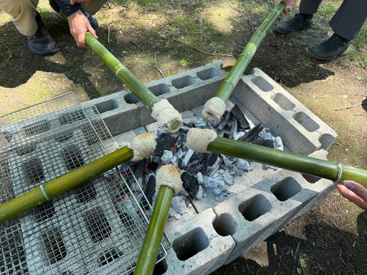 火を囲む竹に巻きつけたどんぐりパン