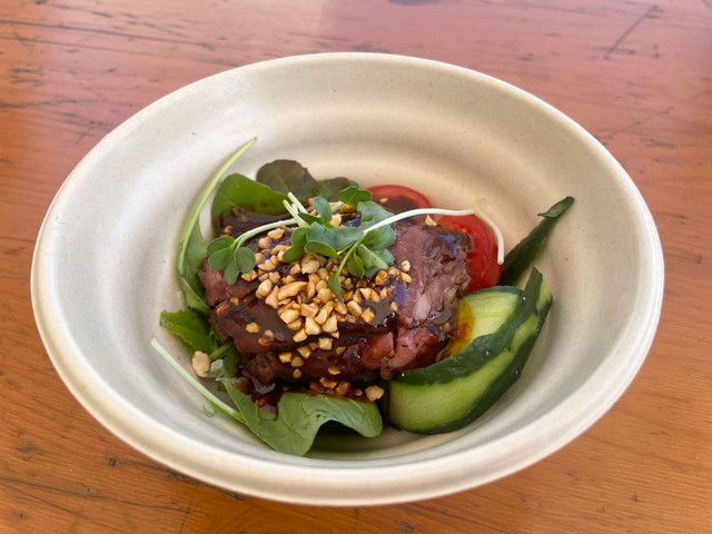 赤坂四川飯店の口水牛肉（よだれ牛）。白い器にルッコラやトマト、きゅうりと共に牛肉が盛られ、砕いたナッツと濃厚なタレがかかっている
