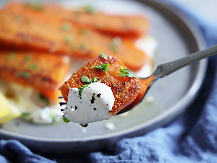 フォークでヨーグルトソースを絡めた焼きにんじん一切れをすくい上げている寄りの写真