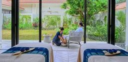 フサキビーチリゾートのスパ室内で施術台2台が並び、セラピストと利用者が向かい合って座り、大窓から緑の庭園が見えるスパ空間の写真