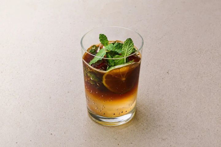 グラスに注がれたアイスコーヒーカクテル。ライムスライスとフレッシュミントをトッピングし、上層が濃い茶色・下層がオレンジ色に分かれた2層グラデーションのコールドドリンク
