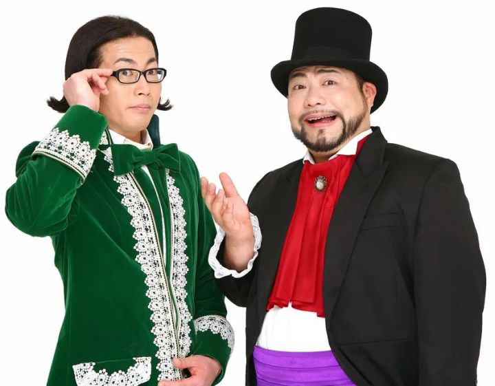 黒トップハットと赤スカーフ衣装の男性と緑ベルベットジャケット衣装の男性2人が並んで立つ宣伝用人物写真。イベントMCまたは出演者と思われる