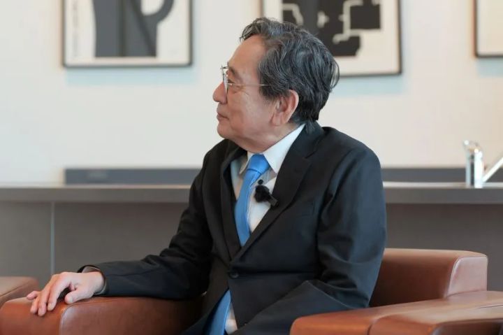 黒スーツに青ネクタイ姿の男性がソファに座り、横を向いて発言している対談中のポートレート写真