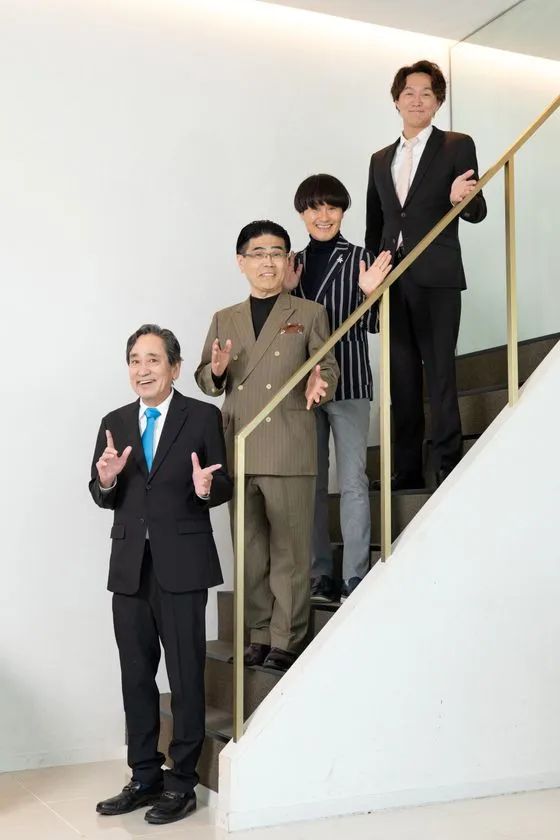階段上で4名の出席者がカメラに向かってポーズを取る集合写真。ルー大柴氏（青ネクタイ）を含む異業種参加者4人が並ぶ