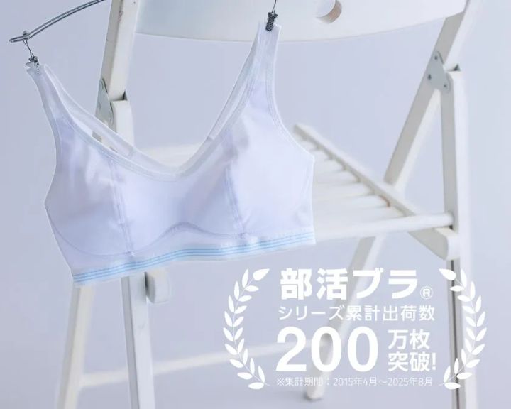 白いスポーツブラ（部活ブラ）をハンガーに吊るした商品写真。下部に部活ブラシリーズ累計出荷数200万枚突破のテキストロゴ入り（集計期間2015年4月〜2025年8月）