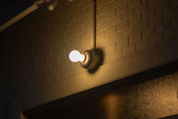 CAST ALUMINUM LAMPをレンガ壁面に取り付けた点灯状態の設置例。アルミ鋳物製ブラケット本体と電球が壁から張り出した実際の使用シーンを暗所で撮影。